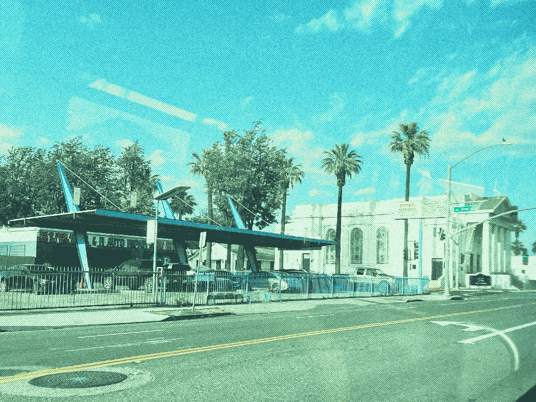a car wash with tall, angled  canopy support pylons. A large stone building can be seen behind it.