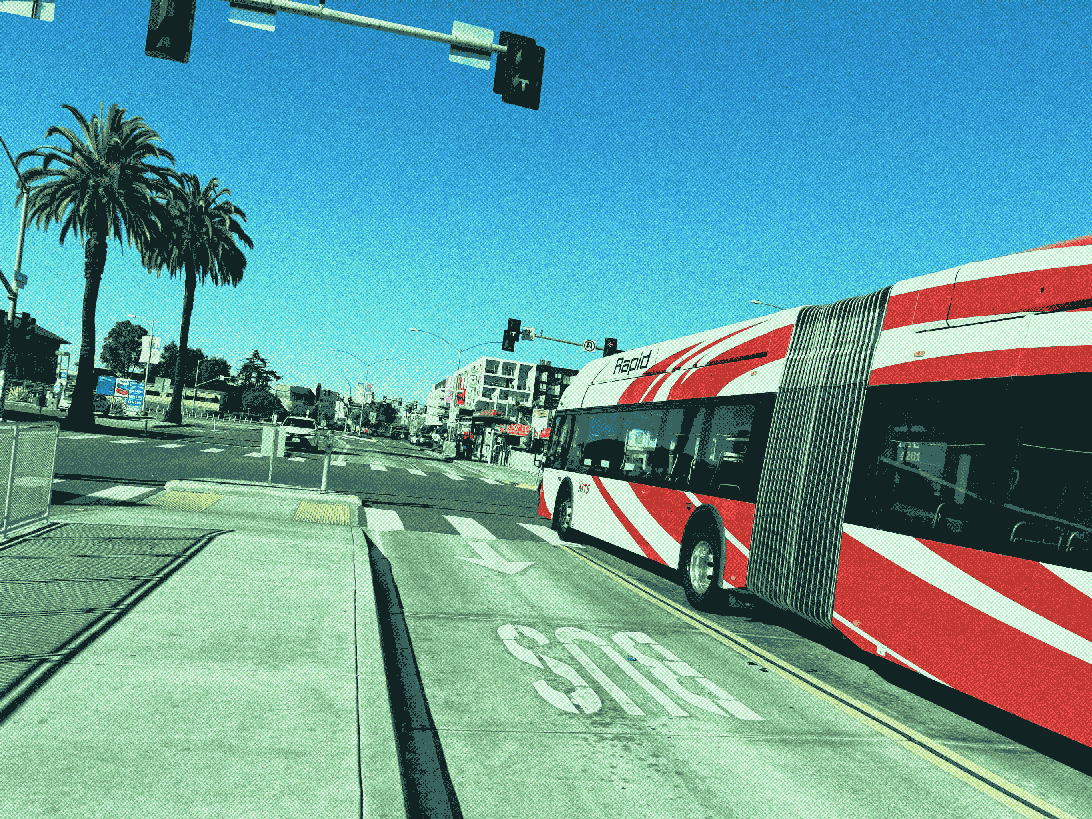 articulated MTS bus crossing a street. it does not have any doors on the drivers side. there are aspect signals on the traffic signal mast arm