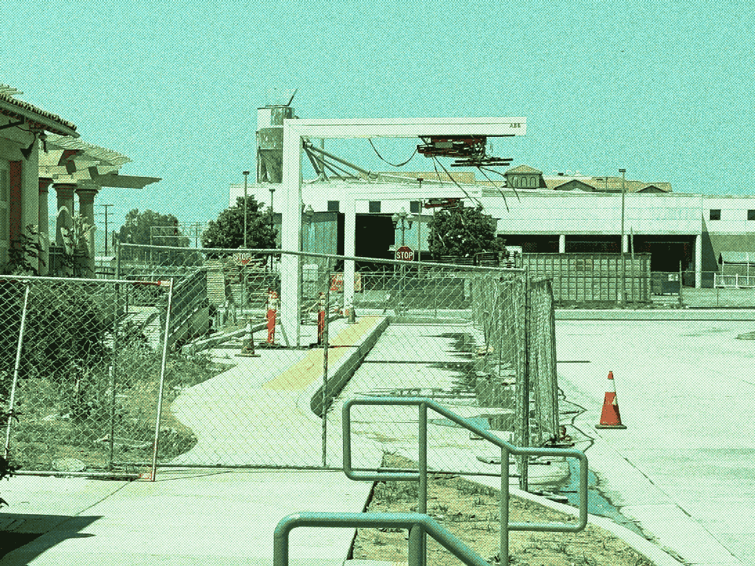 two overhead charging devices of rectangular shape over a curb next to a stucco building with wooden pergolas